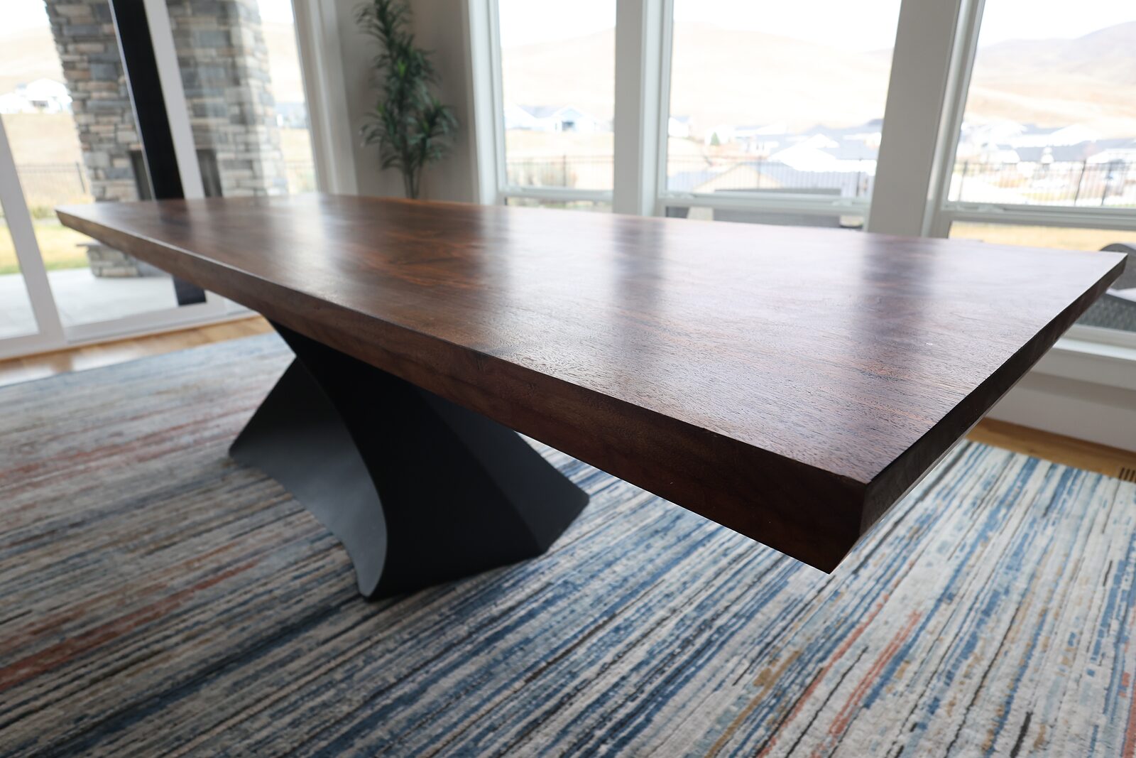 Ten-foot live-edge walnut dining table on a sculpted black steel base, in front of floor-to-ceiling windows